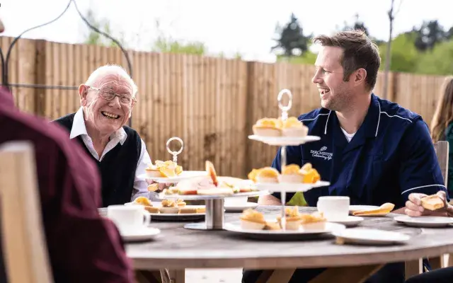 A nursing care home resident and nurse eating cake together